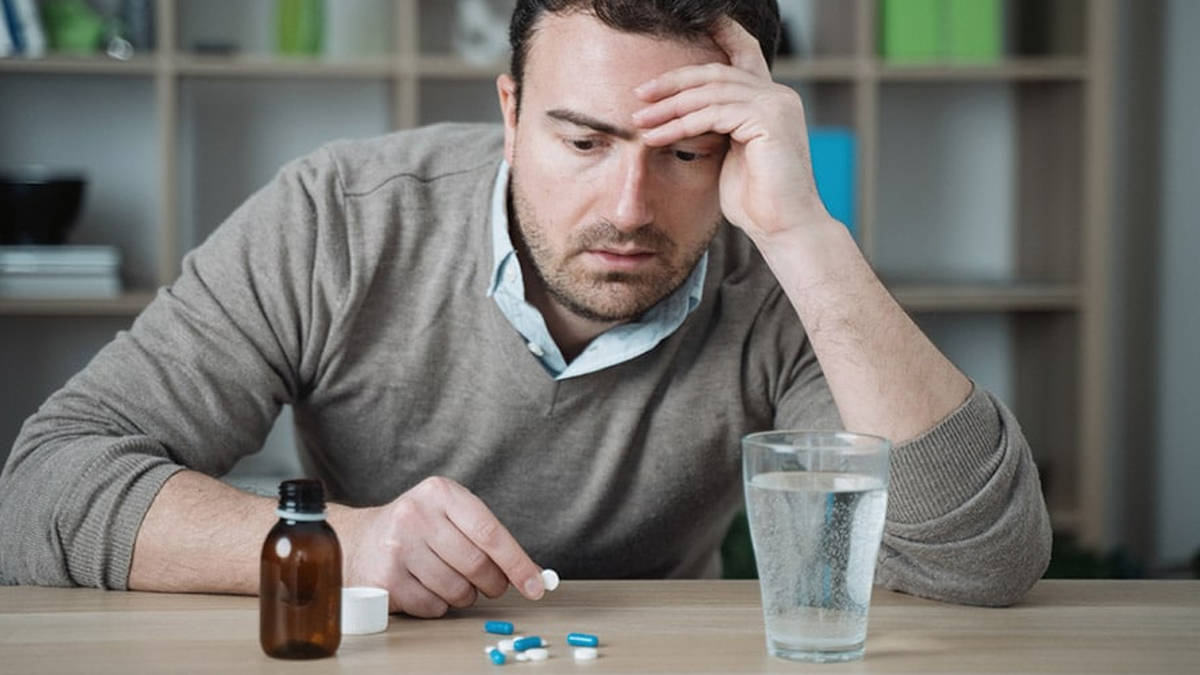 Man staring at a pile of pills with his head resting in his hand. Long-term benzodiazepine use can lead to psychological dependence.