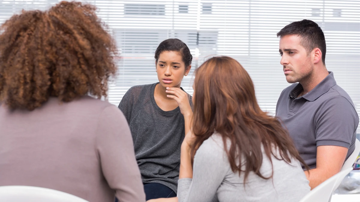 Group of adults sitting in a circle and listening intently to each other. Treatment for alcohol addiction includes group therapy.