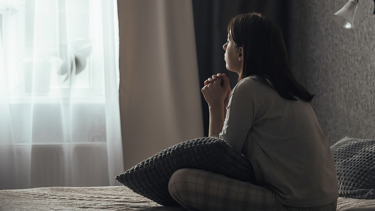 Woman on a bed looking out a window in a dark room. White text explains that seasonal affective disorder (SAD) is a type of depression.