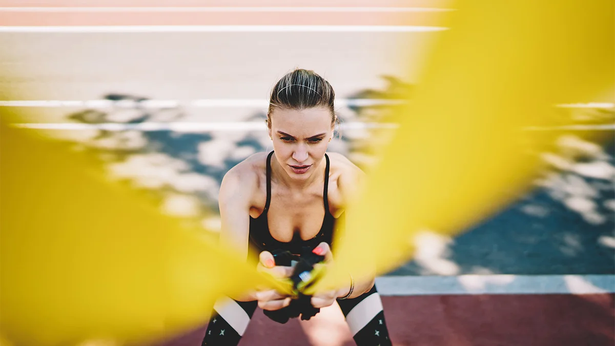 A woman is engaged in an intense exercise, pulling resistance bands in an outdoor setting.