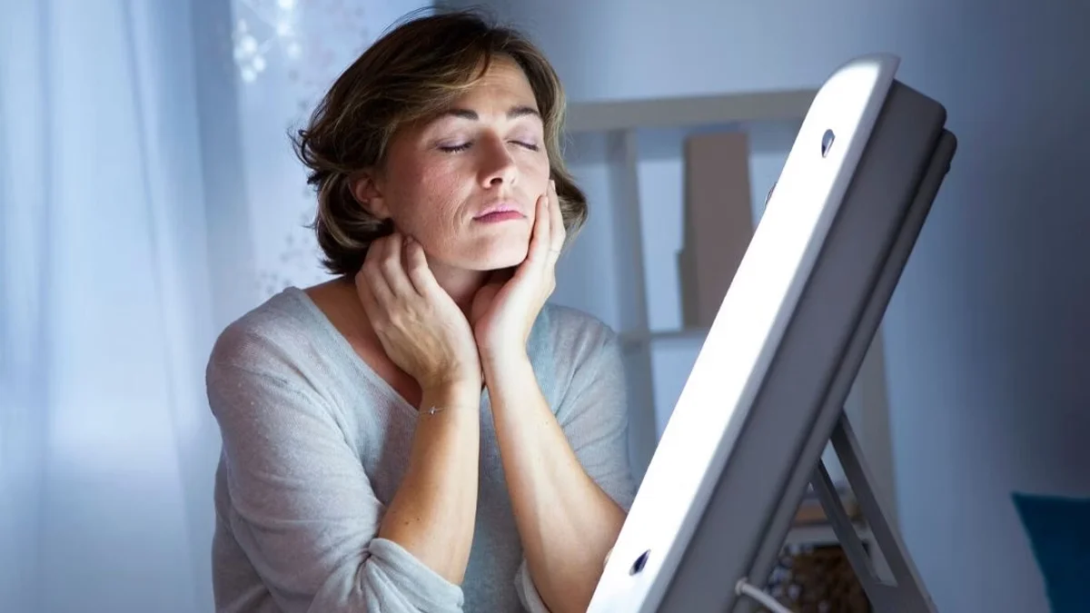 Woman sitting in front of a light therapy box.